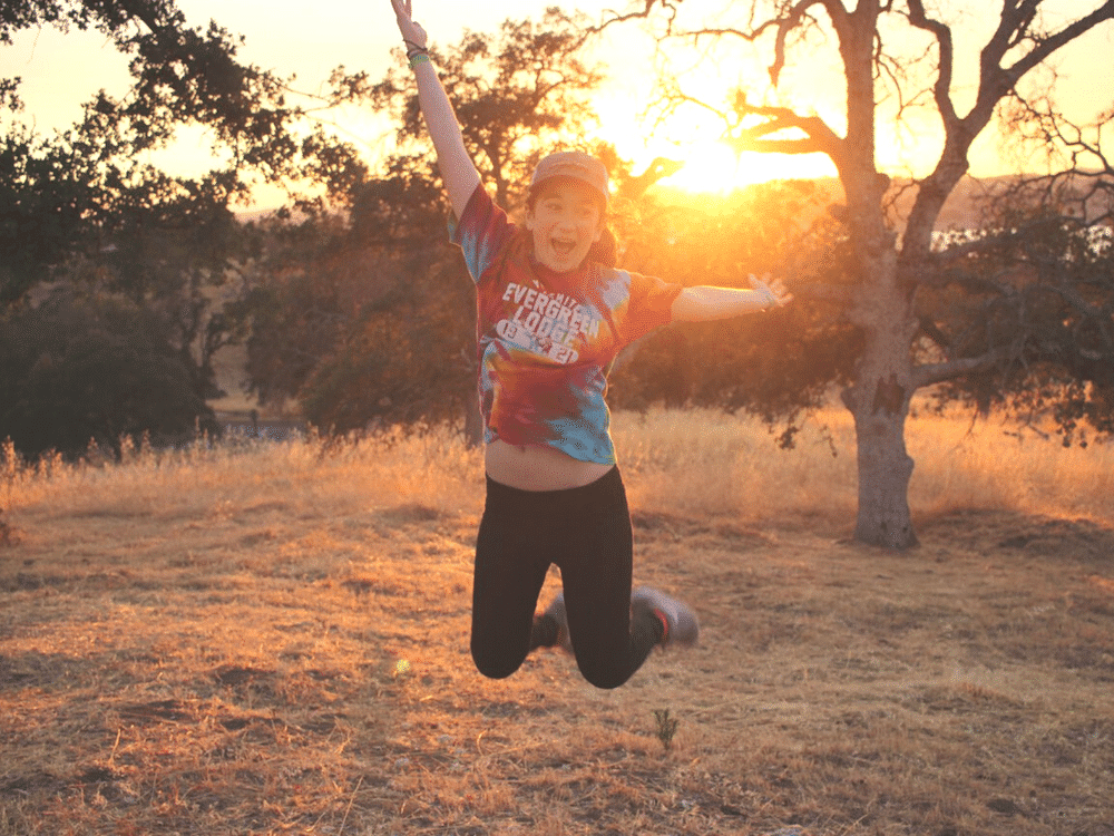 Girl jumping and smiling at sunset in woods